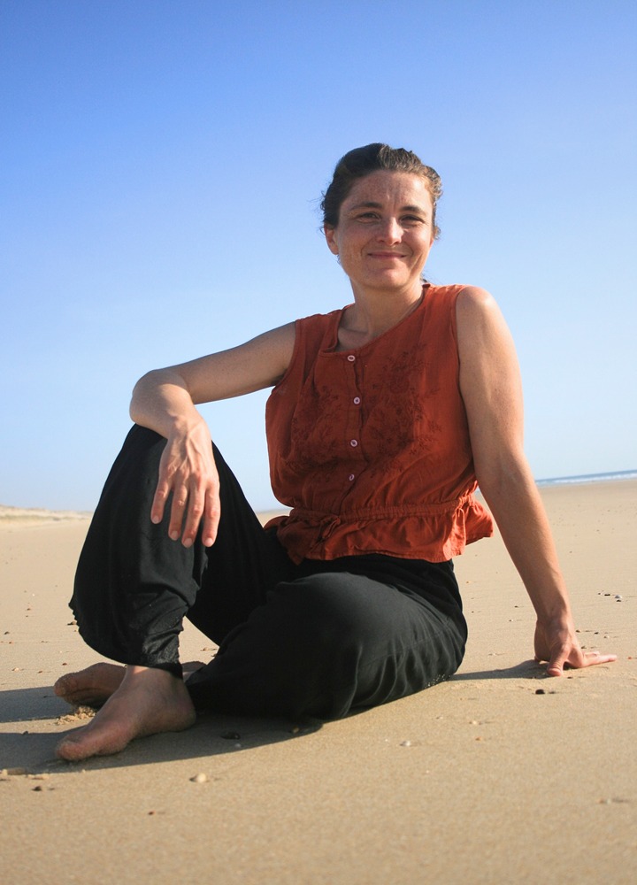 Amandine Désétables, assise en tailleur sur une plage, souriante, vue en pied